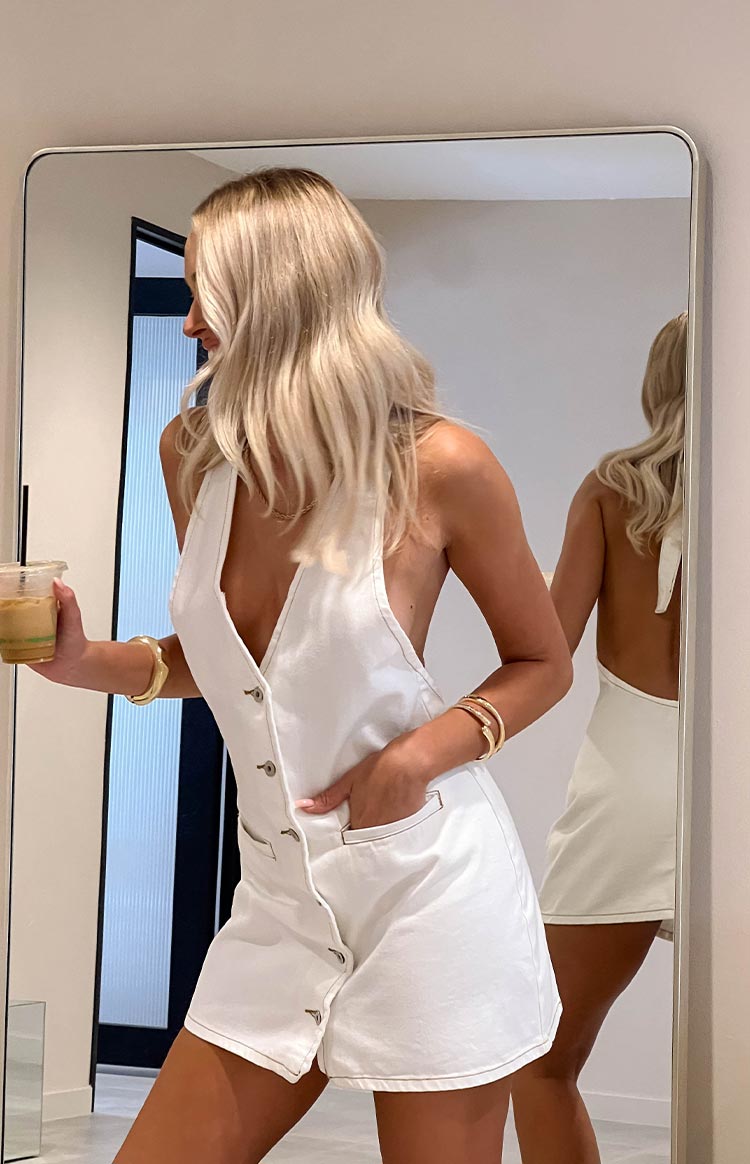 Side view of a white denim halter neck mini dress with deep V-neck and button front, showing the open back in the mirror reflection