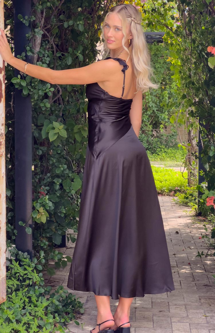 Side-rear view of a black satin maxi dress with a ruffled shoulder detail and a full, flowing skirt