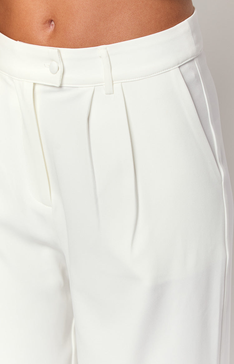 Close-up of the white tailored pants showing the front pleats, button closure, and side pocket