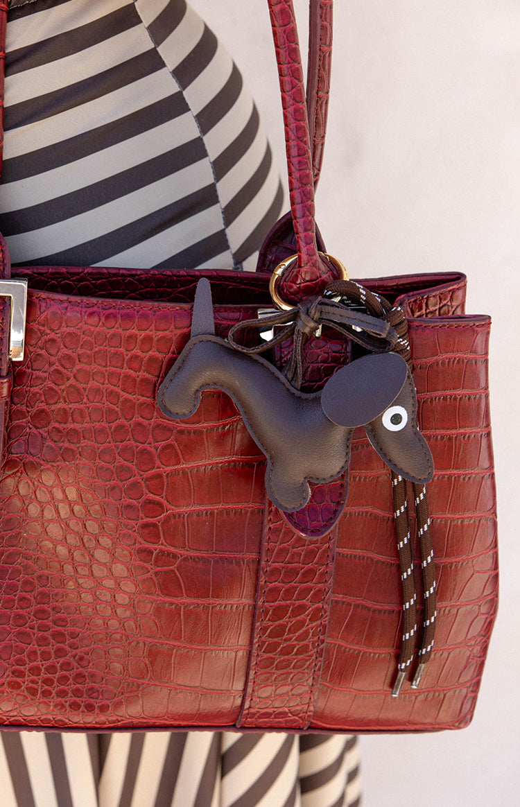 Black leather dachshund bag charm with white eye detail hanging from a red bag by a braided cord