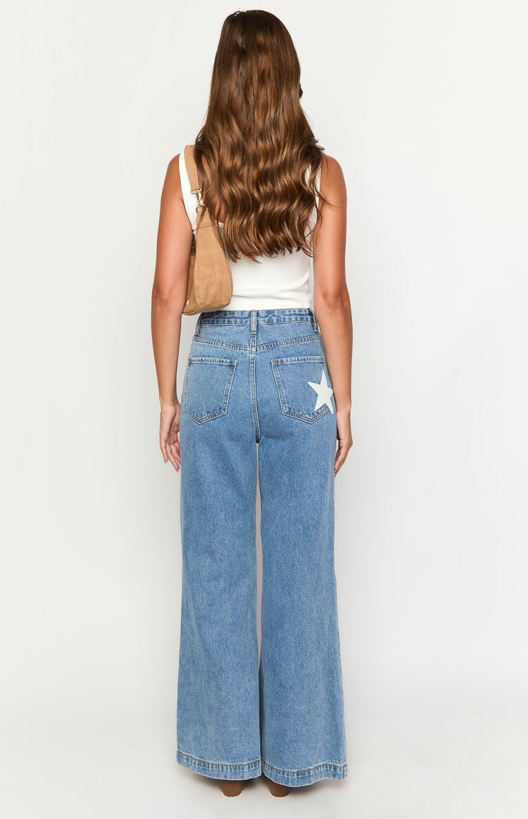 Rear view of mid wash denim flare jeans with a white star detail on the right back pocket and classic back pockets