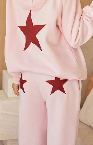  The back view of light pink sweatpants featuring large dark red star appliques on each back pocket.