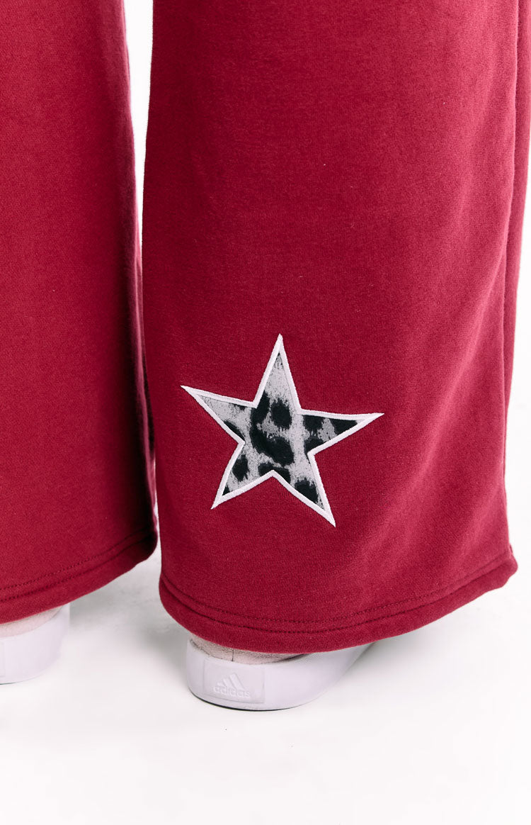 Close-up of the white-outlined leopard print star appliqué on the lower leg of burgundy track pants