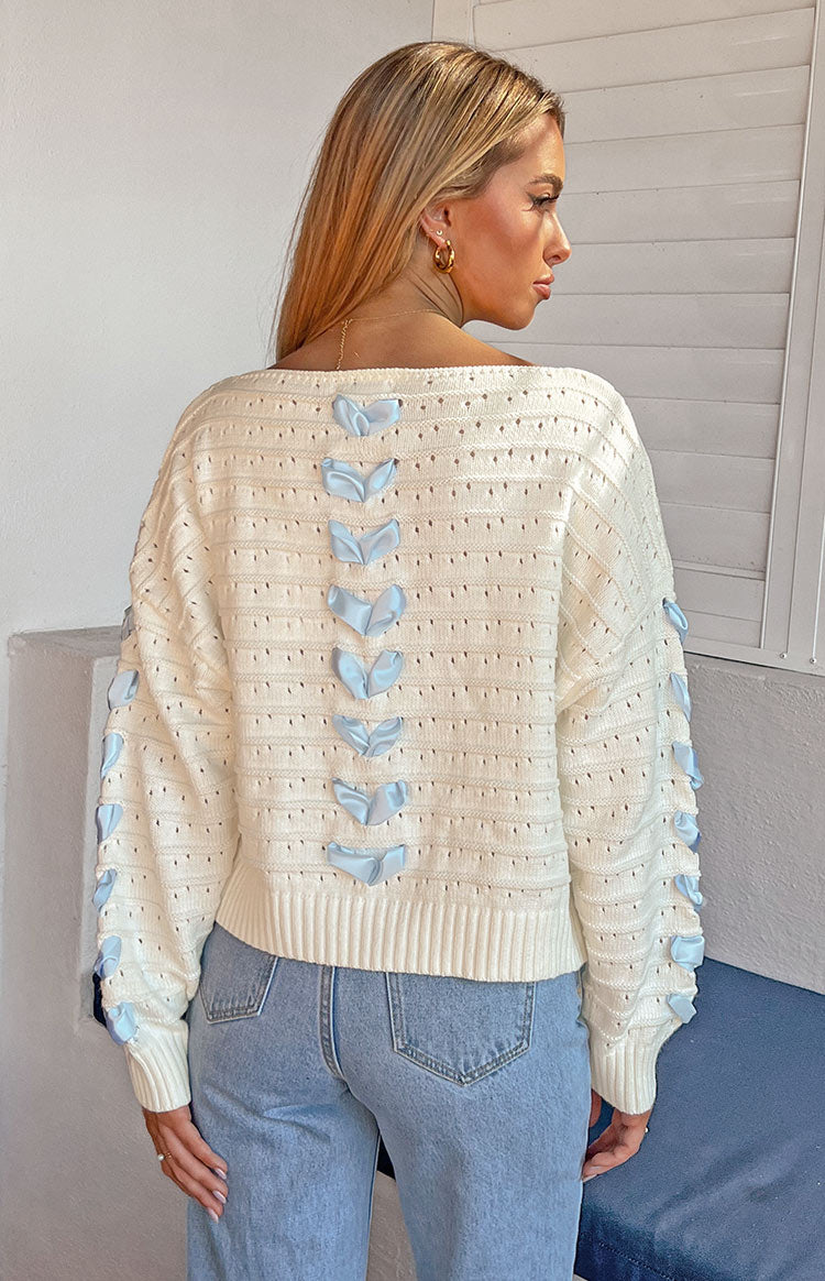 Rear view of the white knit sweater with a boat neck and light blue satin ribbon details on the back and sleeves