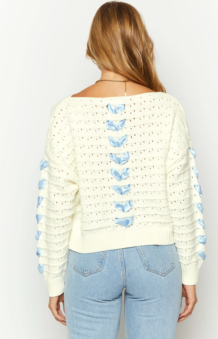 Rear view of an off-white open knit sweater with light blue satin ribbon bows tied down the center back and along the long sleeves