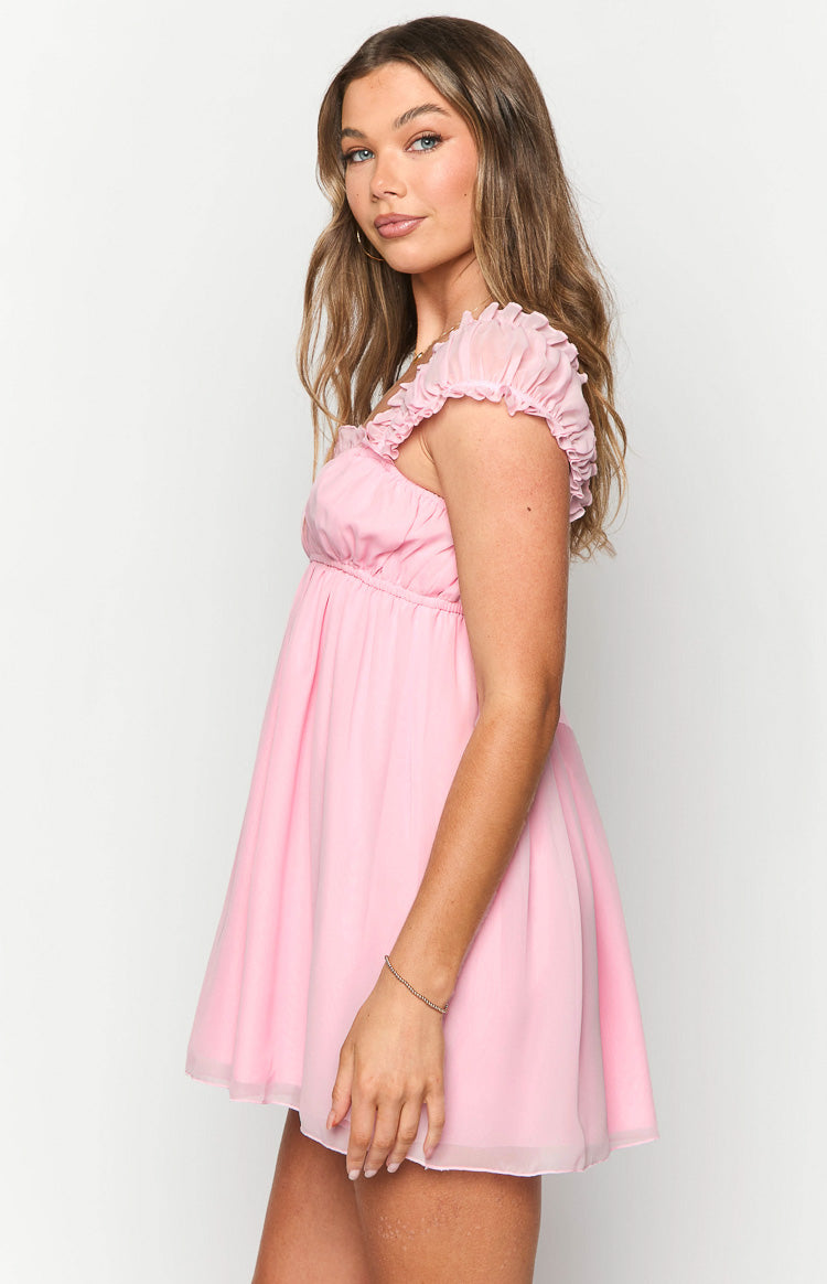 Side view of a pink mini dress with ruched short sleeves and an empire waist flowing into a layered skirt