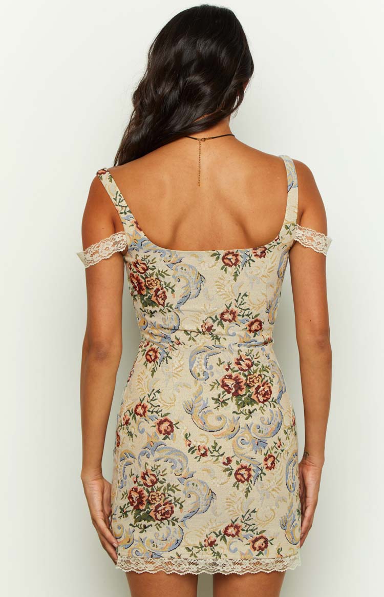 Rear view of a beige tapestry mini dress with a square back, off-shoulder lace trim, floral pattern, and lace hem