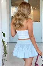 Rear view of a light blue mini skirt with a flat waistband and a gathered ruffle hem