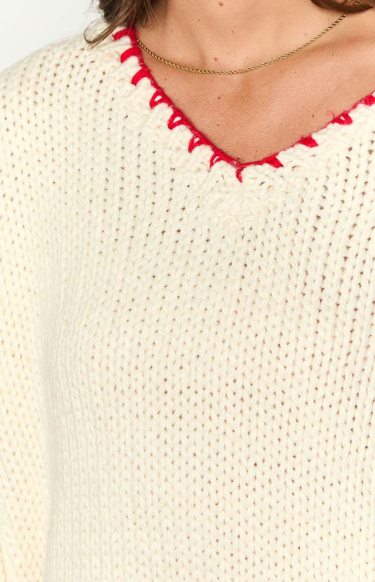 Close-up of the cream chunky knit sweater showing the red contrast stitch V-neck
