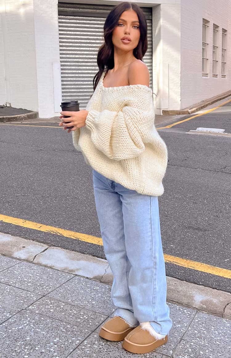 Side view of a cream chunky knit sweater with a wide off-shoulder neckline and voluminous balloon sleeves