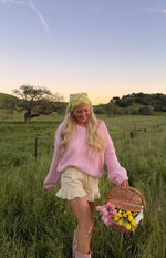 Light pink chunky knit sweater with a relaxed fit, V-neck, dropped shoulders, and wide cuffs
