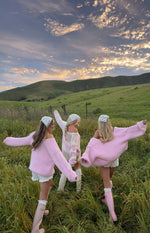 Rear view of a light pink chunky knit sweater worn off-shoulder with wide long sleeves and a relaxed fit
