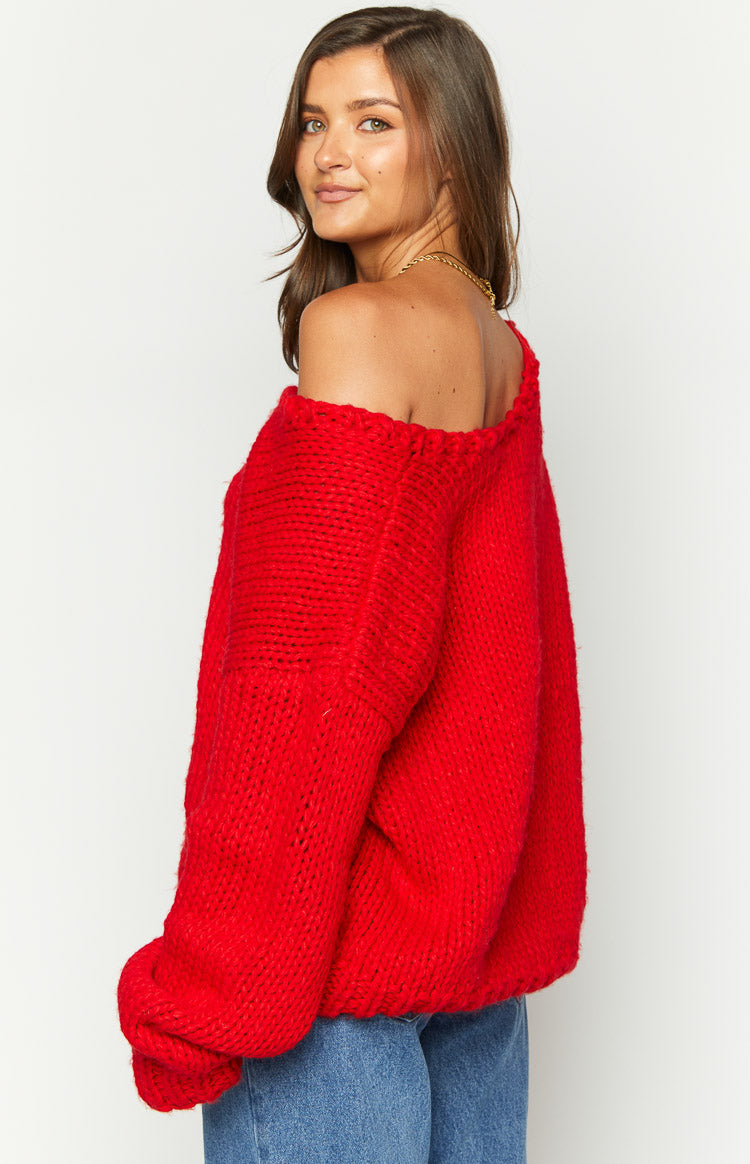 Side view of a red chunky knit sweater with an off-shoulder neckline and voluminous long sleeves