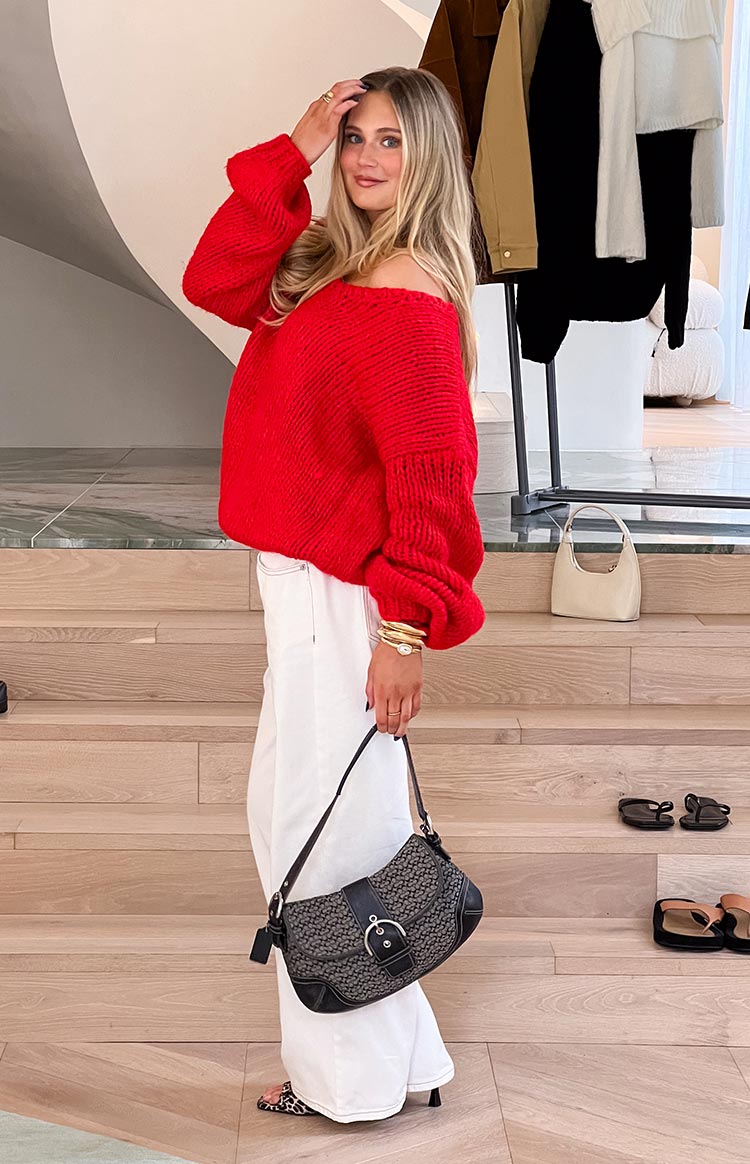 Side view of a red chunky knit sweater with an off-shoulder neckline and voluminous long sleeves