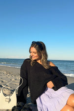 Oversized black chunky knit sweater with a wide neckline worn off one shoulder, highlighting the textured knit