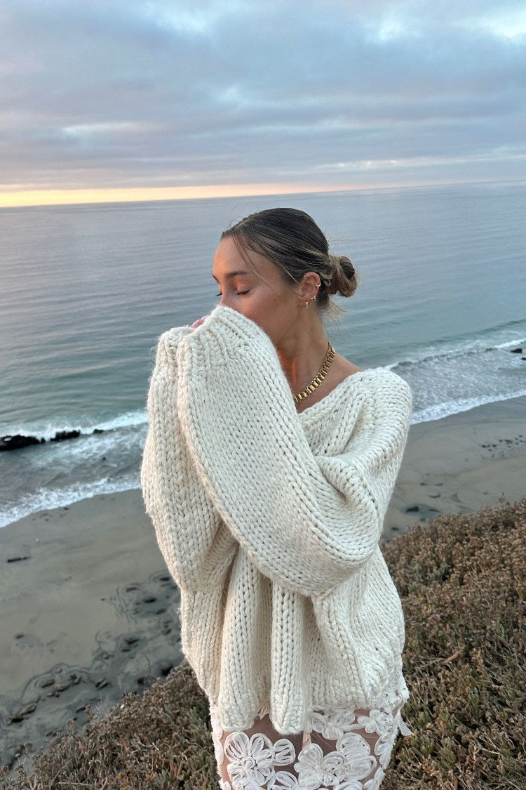 Cream chunky knit sweater with an oversized fit, wide V-neck, and long, voluminous sleeves