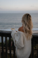 Side view of a cream chunky knit sweater with an off-shoulder neckline and voluminous long sleeves