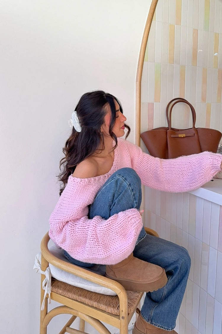 Side view of a light pink chunky knit sweater with an off-shoulder neckline and long oversized sleeves