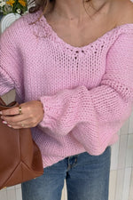 Close-up of a light pink chunky knit sweater showing the wide V-neck with open knit detail and voluminous sleeves