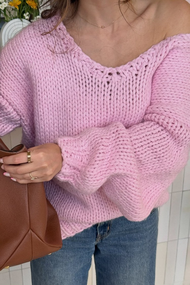 Close-up of a light pink chunky knit sweater showing the wide V-neck with open knit detail and voluminous sleeves