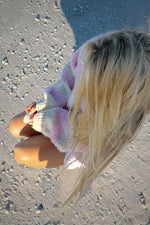 Close-up overhead of a pink, purple, and white striped chunky knit sweater with wide ribbed cuffs