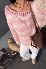 Close-up of a pink and white striped chunky knit sweater with a wide boat neckline and distressed hem