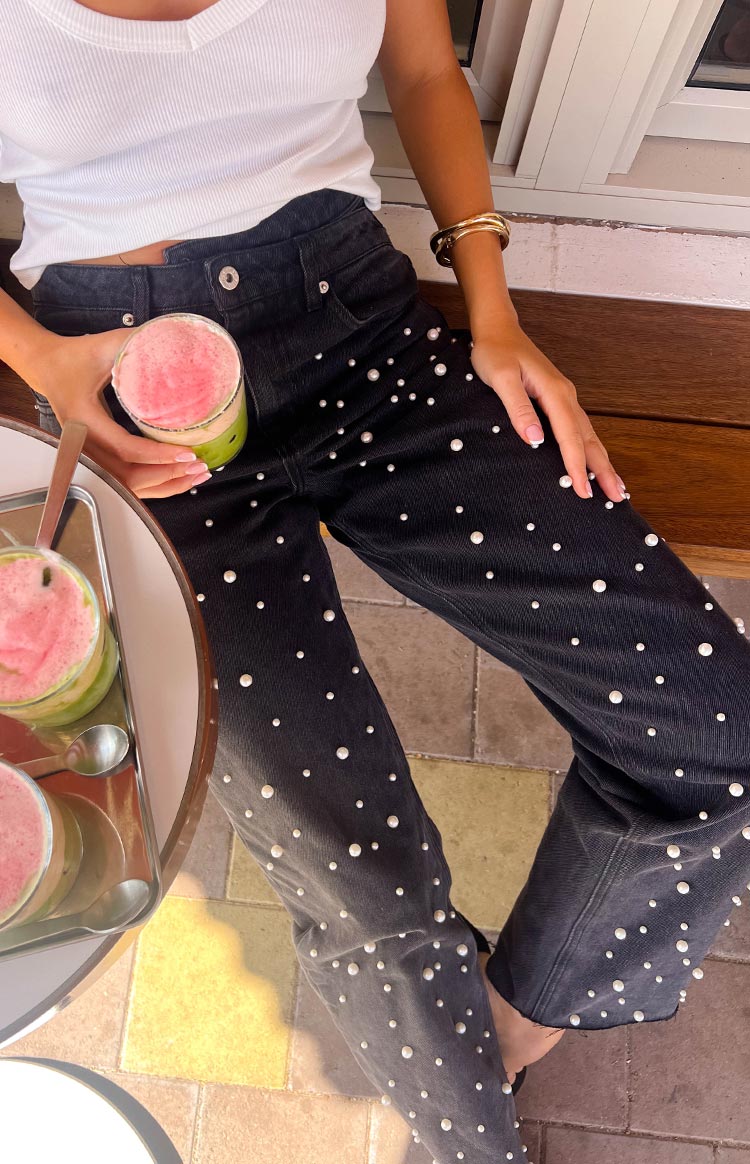 Top-down view of black high-waisted jeans with scattered pearl embellishments on the legs