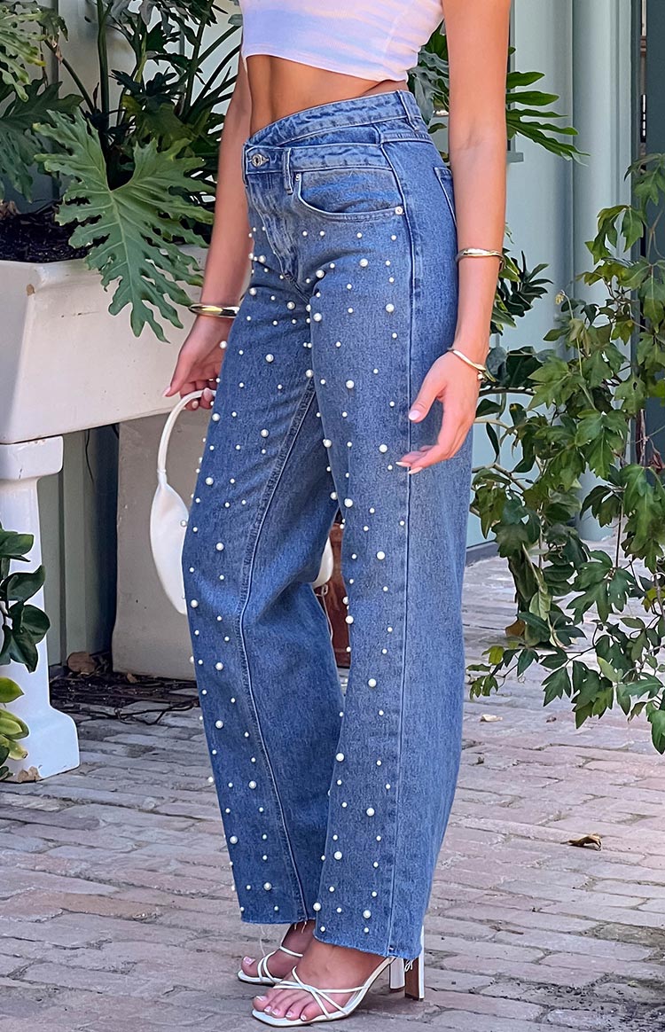 Side view of mid wash denim high waisted jeans with scattered pearl embellishments and raw hem