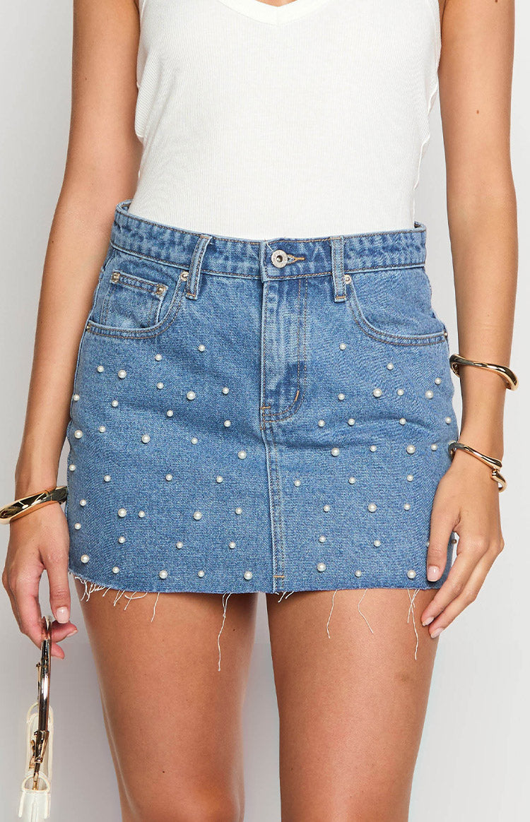 Front view of a mid wash denim mini skirt covered in scattered pearl embellishments with a frayed raw hem