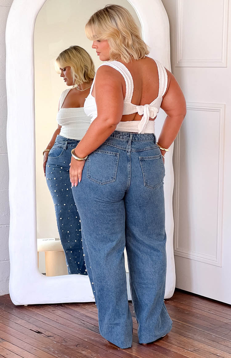 Rear view of mid wash high waisted jeans with back pockets and pearl embellishments visible in reflection
