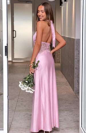 The back view of a light pink satin halter gown- showcasing a sheer lace insert at the back of the bodice and a graceful flow to the skirt. This dress is ideal for a gala or a sophisticated evening event.
