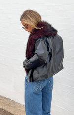 Side view of a black PU jacket with a fluffy burgundy fur collar and cropped hem