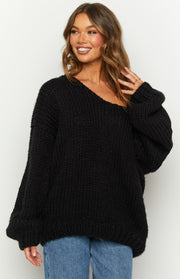 Close-up of the black chunky knit sweater showing the wide off-the-shoulder neckline and voluminous sleeves