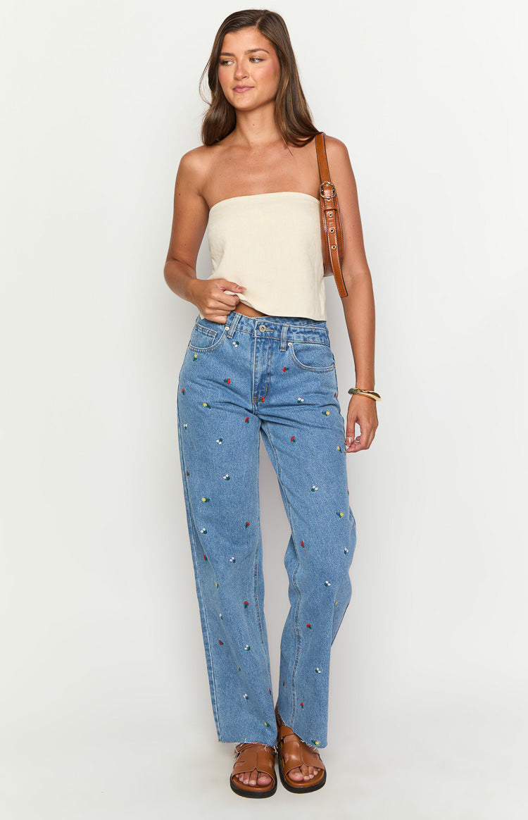 Full length front view of blue denim jeans with all-over colourful embroidery and an uneven high-rise waist