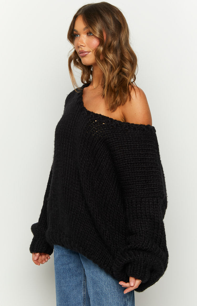 Side view of a black chunky knit sweater with an off-shoulder neckline and oversized long sleeves