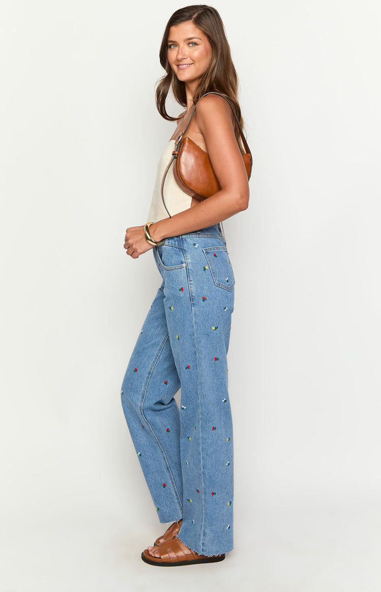 Side view of light blue straight leg jeans with all-over colourful floral embroidery and uneven waist