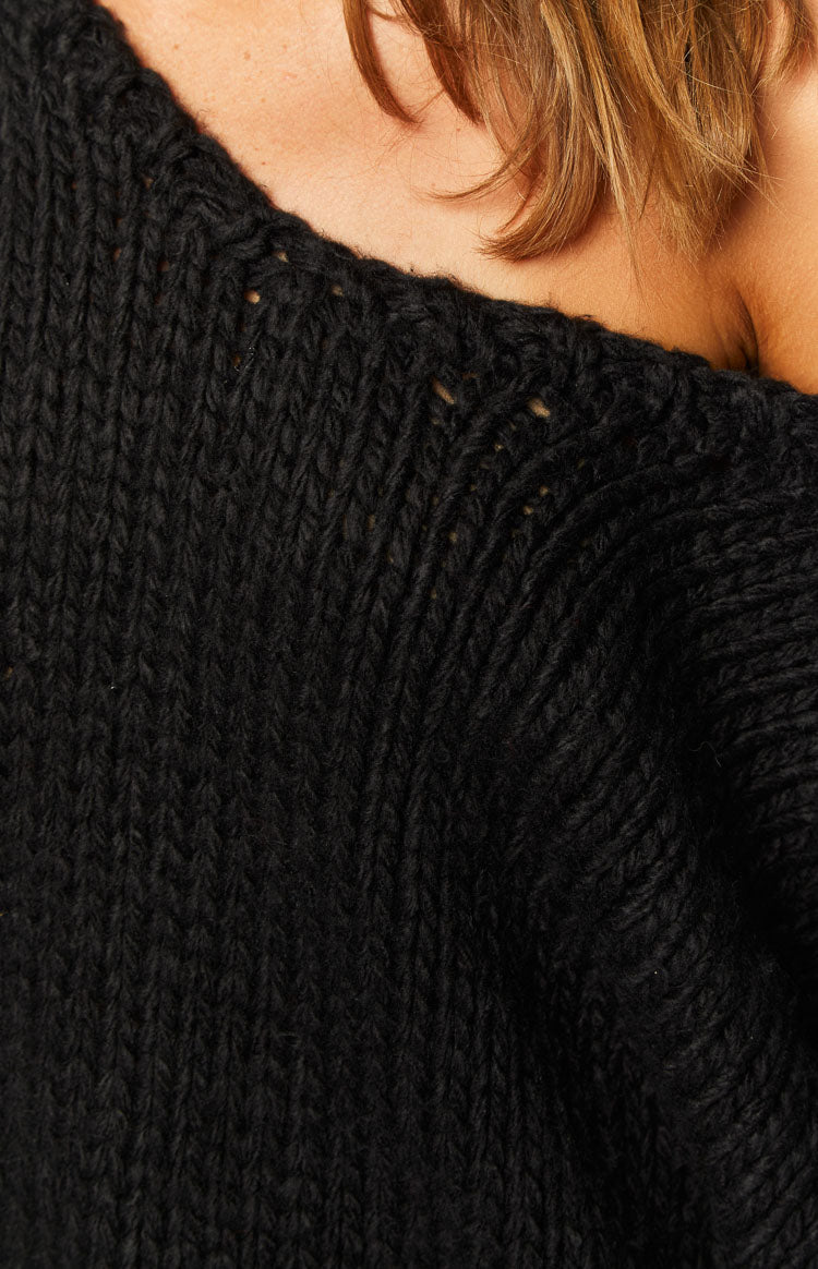 Detail of the black chunky knit sweater's off-shoulder neckline and thick knit texture