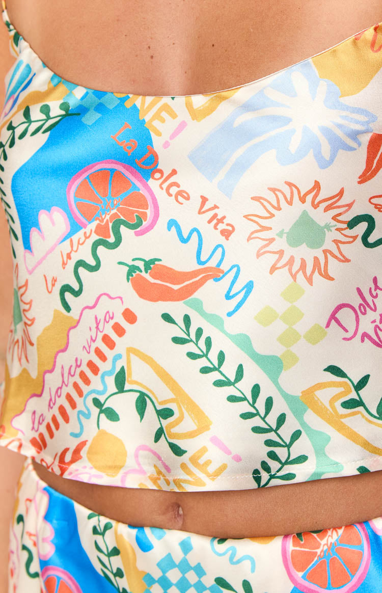 Close-up of the white satin crop top with a colourful La Dolce Vita print featuring lemons chili peppers and leaves