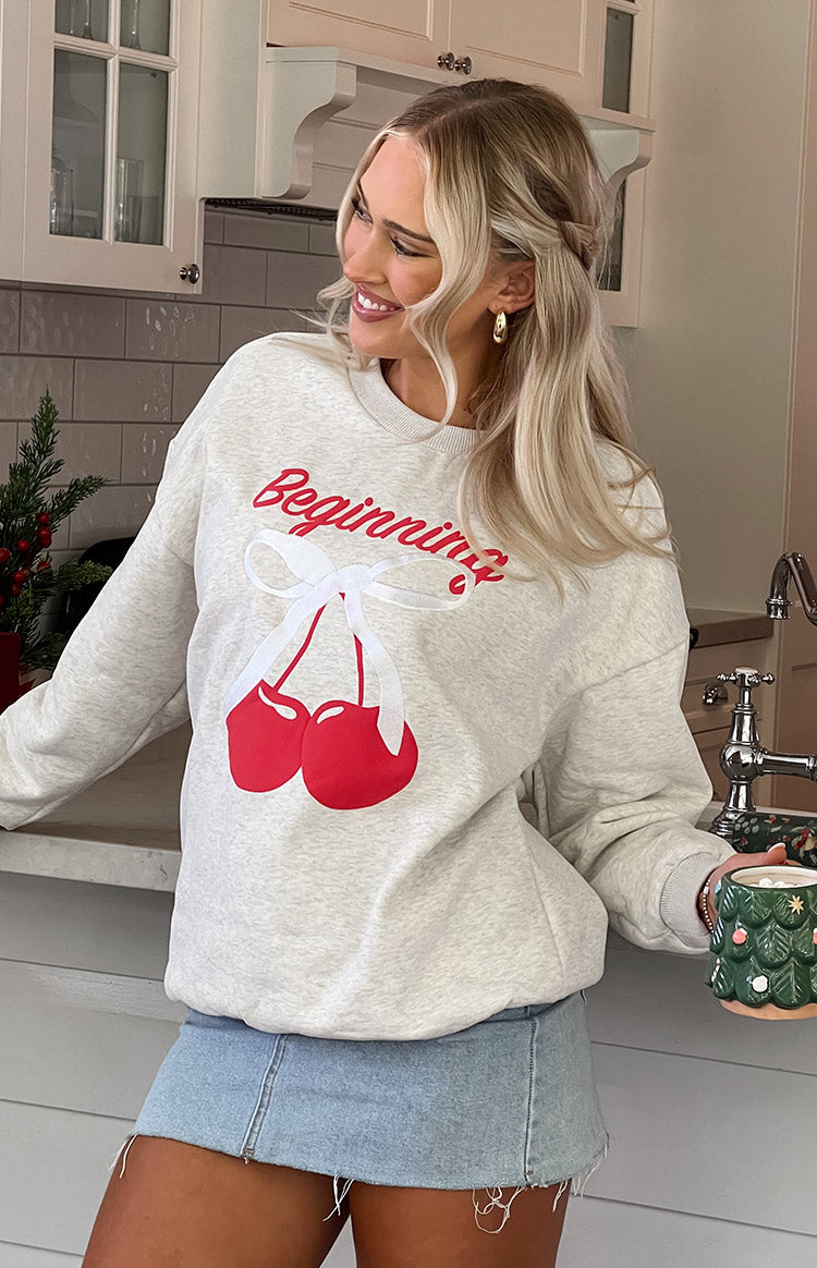 Close-up of the oat marle crew neck sweater with red 'Beginning' text and cherry graphic