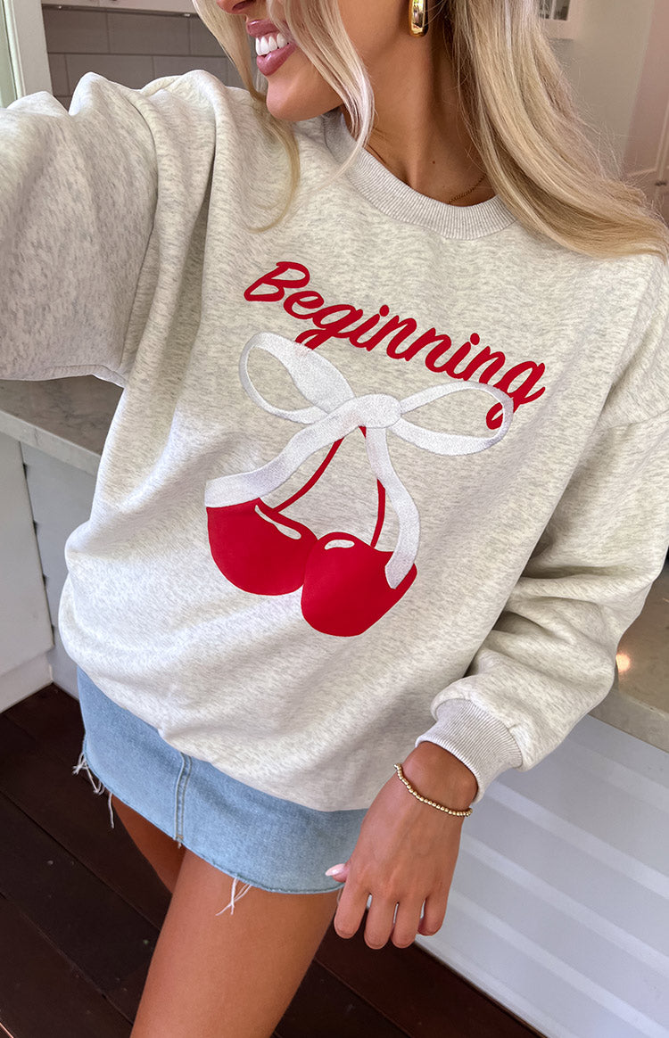 Close-up of the oat marle crew neck sweater showing the red 'Beginning' text and cherry graphic with white bow