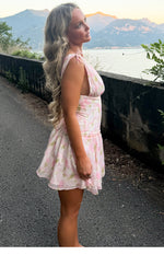 Side view of a pink floral mini dress with tie-shoulder straps, deep armholes, and a ruched waist leading to a flowy tiered s