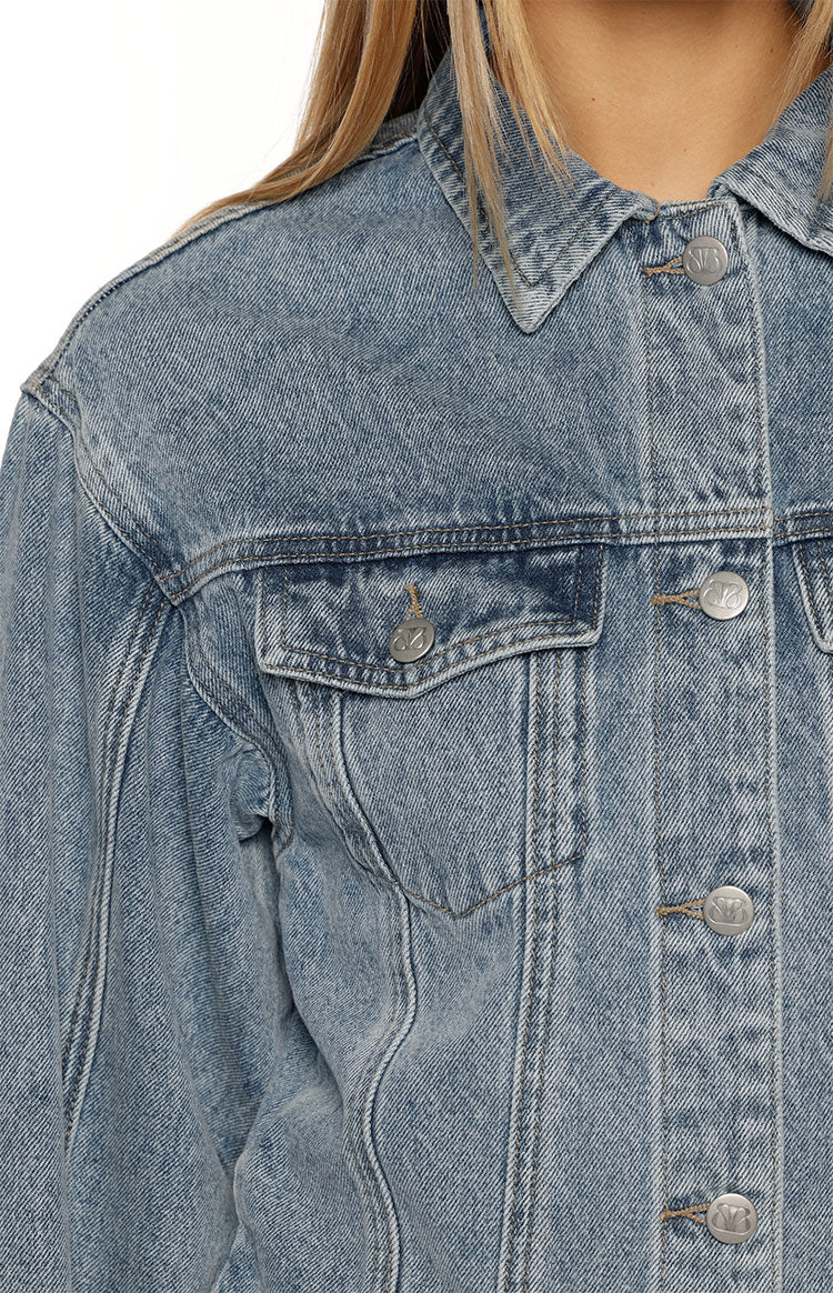 Close-up of the mid-wash denim jacket showing the chest pocket with flap and silver button placket