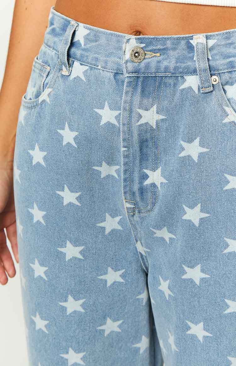 Close-up of the mid wash denim jeans showing the button closure, zipper fly, and white star print pattern