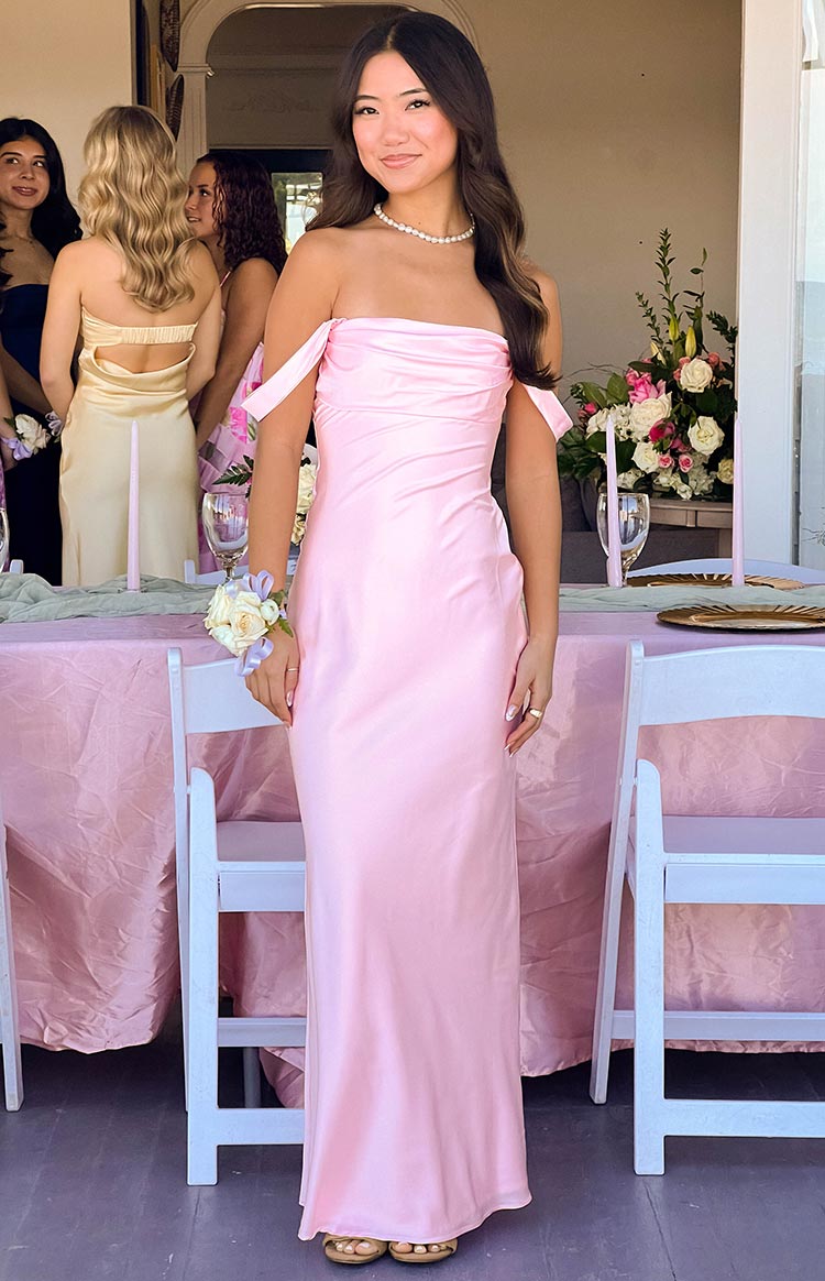 Full length front view of a light pink satin off-shoulder maxi dress with a draped neckline and fitted bodice