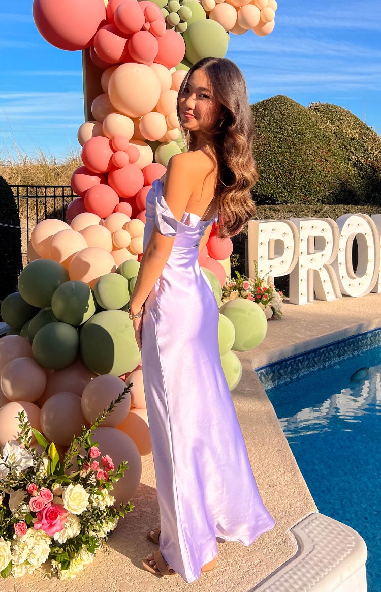 Side profile of the lilac off-shoulder maxi dress, highlighting the draped sleeves and smooth satin fabric