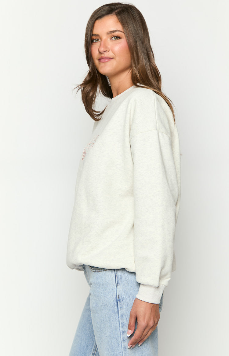 Side view of a relaxed fit light grey marle crew neck sweater with long sleeves and subtle chest embroidery