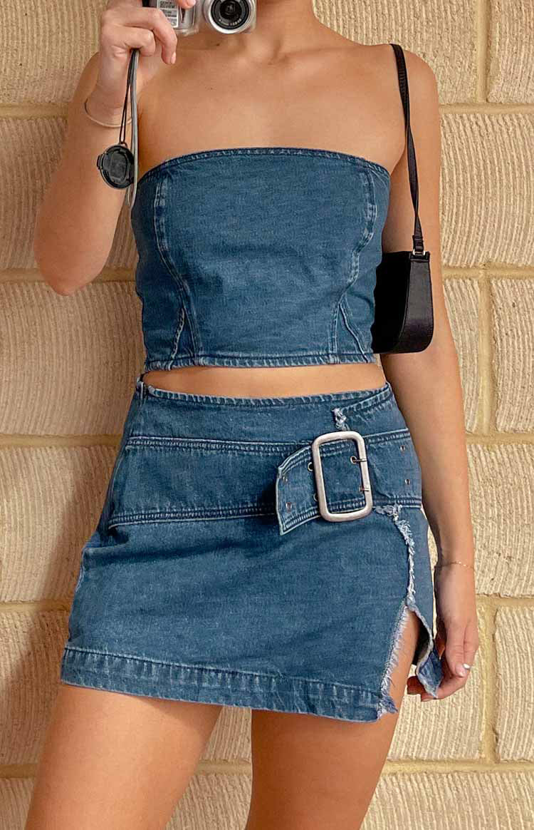 Front view of a blue denim mini skirt with a large silver buckle and a frayed side slit