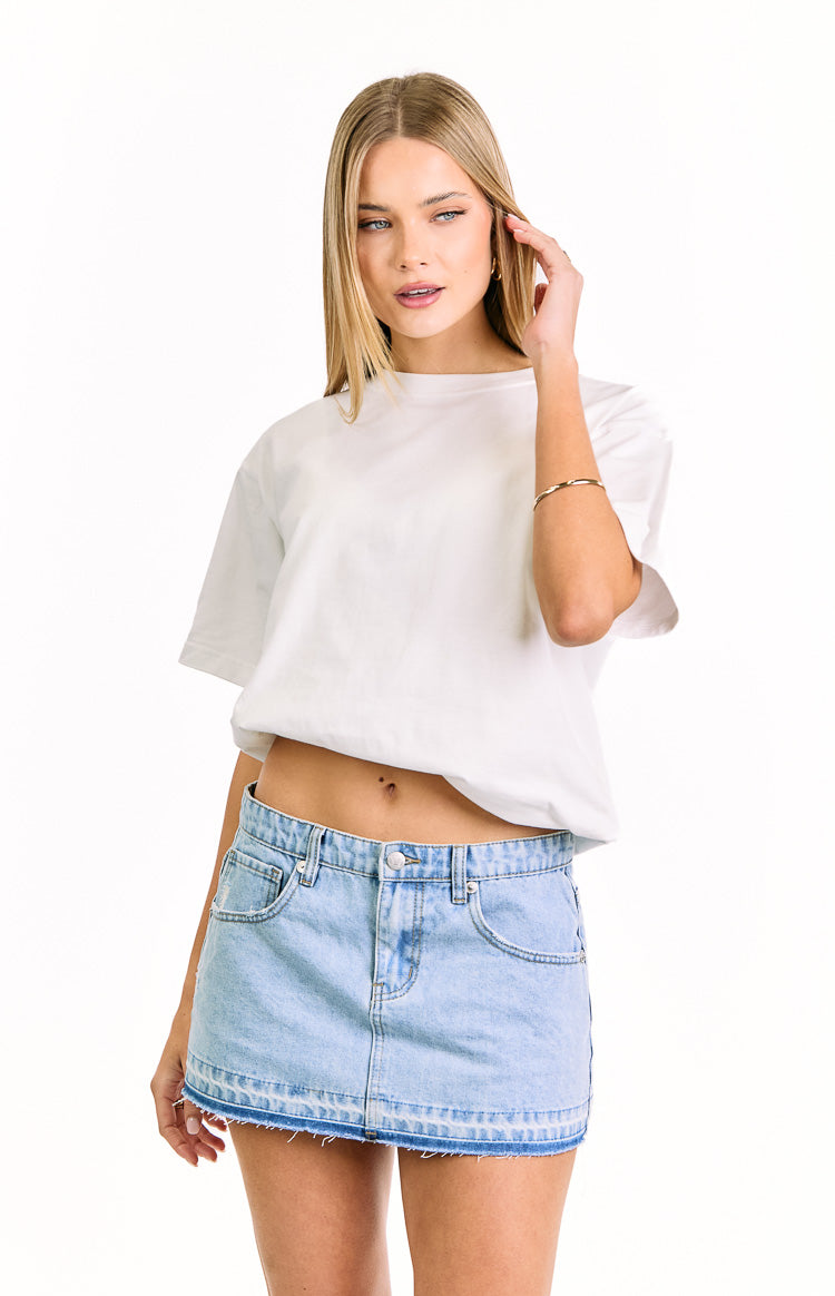 Light wash denim mini skirt with a distressed raw hem, front pockets, and button and zip closure