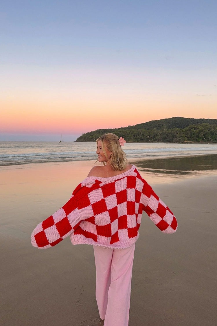Rear view of an oversized pink and red checkered chunky knit cardigan worn off the shoulders