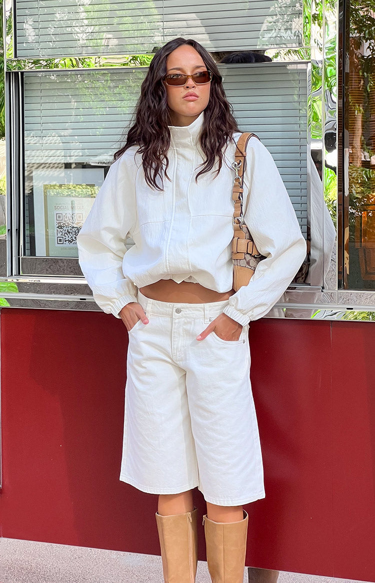 Front view of a cream funnel neck sports jacket with a full zip, cropped length, and elasticated hem and cuffs